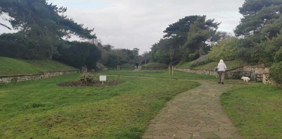 Woman walking her dog along a path with grass.